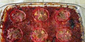 Ένα ταψί με Μελιτζάνες με ρεβίθια, έτοιμο για ψήσιμο, με τη σάλτσα από πάνω και τις ροδέλες ντομάτας.