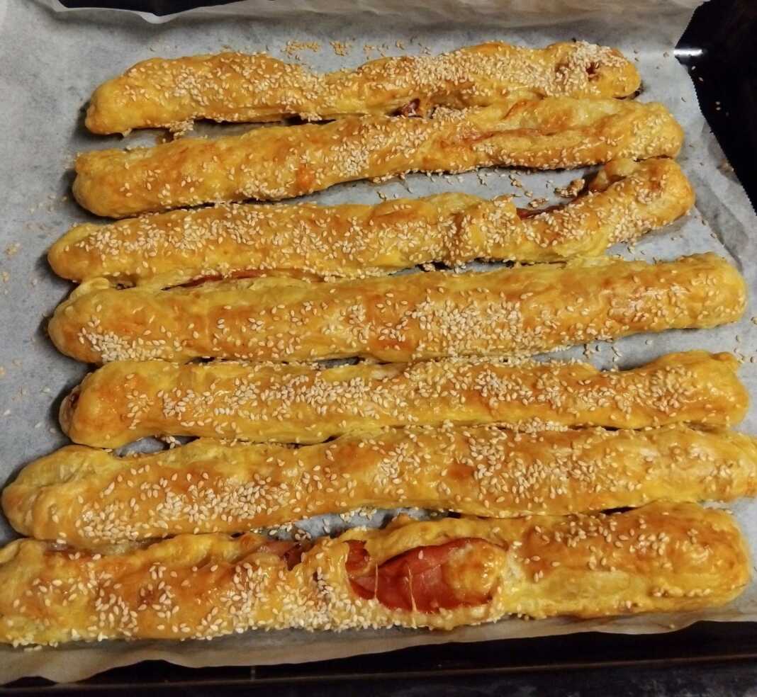 Ταψί με Σφολιατίνια με τυρί και μπέικον, έτοιμα για ψήσιμο, αλειμμένα με αυγό και πασπαλισμένα με σουσάμι