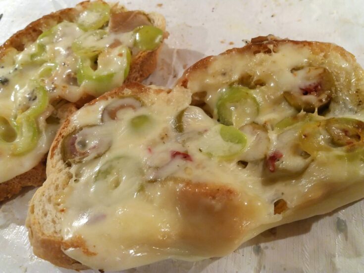 Ένα πιάτο με σκορδόψωμα στην τοστιέρα, με λιωμένο τυρί και τα υλικά από πάνω, φτιαγμένο από μπαγιάτικο ψωμί