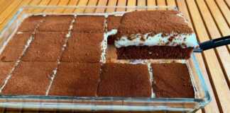 Ένα ολόκληρο σοκολατένιο κέικ με κρέμα και καφέ, πασπαλισμένο με κακάο, σε πιατέλα, έτοιμο για σερβίρισμα