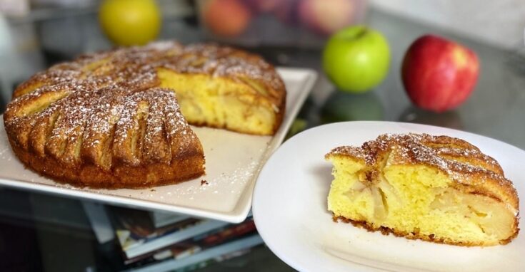 Μια ολόκληρη αφράτη μηλόπιτα με κομμάτια μήλου και πασπαλισμένη κανέλα, σε φόρμα.