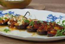 Μια πιατέλα γεμάτη μελιτζάνες γεμιστές με γίγαντες, σκεπασμένες με λιωμένη φέτα και φρέσκο βασιλικό.