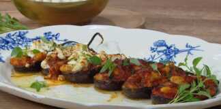 Μια πιατέλα γεμάτη μελιτζάνες γεμιστές με γίγαντες, σκεπασμένες με λιωμένη φέτα και φρέσκο βασιλικό.