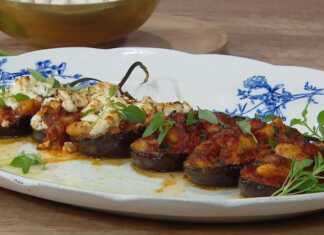 Μια πιατέλα γεμάτη μελιτζάνες γεμιστές με γίγαντες, σκεπασμένες με λιωμένη φέτα και φρέσκο βασιλικό.