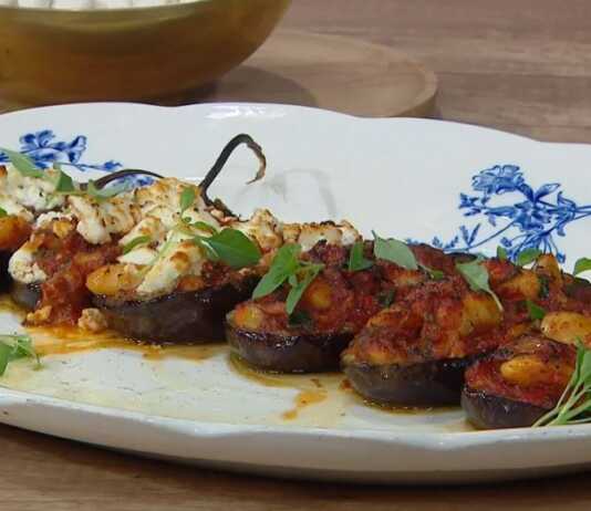 Μια πιατέλα γεμάτη μελιτζάνες γεμιστές με γίγαντες, σκεπασμένες με λιωμένη φέτα και φρέσκο βασιλικό.