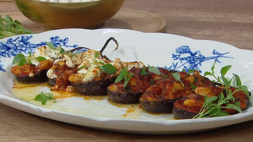 melitzanes me gigantes Μια πιατέλα γεμάτη μελιτζάνες γεμιστές με γίγαντες, σκεπασμένες με λιωμένη φέτα και φρέσκο βασιλικό.