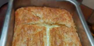 Μια χρυσαφένια τυρόπιτα με μπεσαμέλ, φέτα και κότατζ, κομμένη σε κομμάτια, έτοιμη για σερβίρισμα