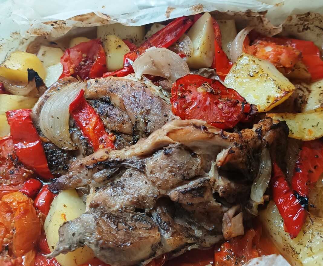 Χοιρινές μπριζόλες μαζί με πατάτες, κρεμμύδια και πιπεριές σε ανοιχτή λαδόκολλα που έχει ψηθεί και έχει πάρει χρώμα