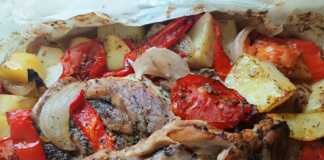 Χοιρινές μπριζόλες μαζί με πατάτες, κρεμμύδια και πιπεριές σε ανοιχτή λαδόκολλα που έχει ψηθεί και έχει πάρει χρώμα