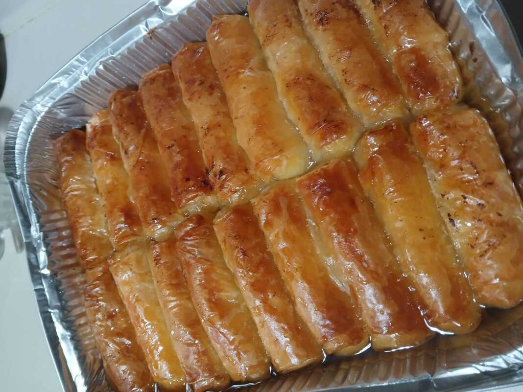 Ατομικά γαλακτομπουρεκάκια σε ρολό με χρυσαφένιο φύλλο κρούστας ποτισμένα με σιρόπι και πασπαλισμένα με κανέλα σε πιατέλα