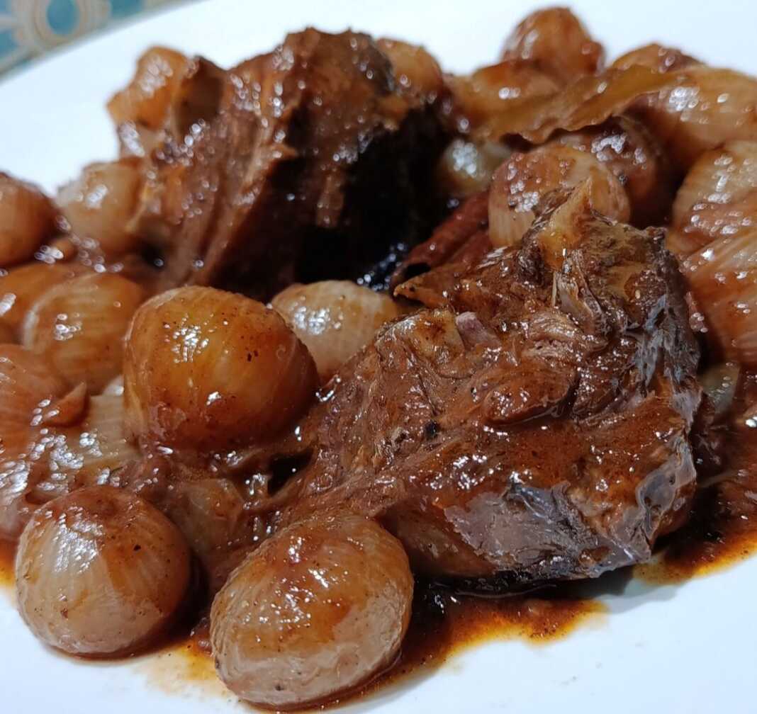 Βαθύ πιάτο με ζεστό Γίδα Στιφάδο με κομμάτια κρέατος και κρεμμυδάκια σε πηχτή κόκκινη σάλτσα