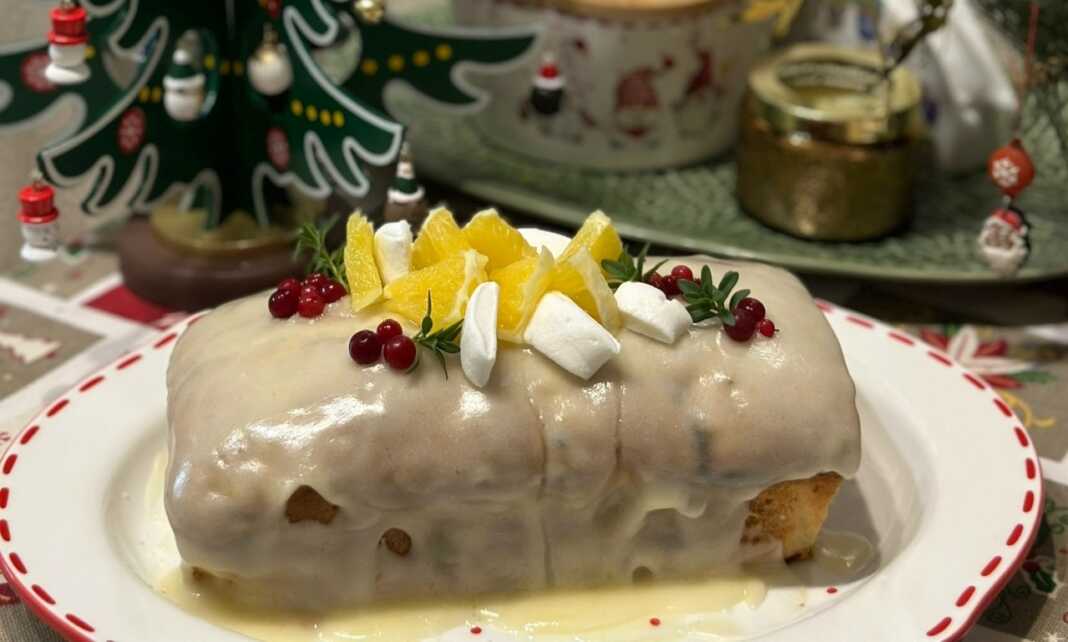 Ένα ολόκληρο μακρόστενο κέικ cranberry με λευκό γλάσο πορτοκαλιού, διακοσμημένο με φρέσκα cranberries και ξύσμα πορτοκαλιού