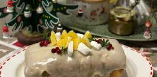 Ένα ολόκληρο μακρόστενο κέικ cranberry με λευκό γλάσο πορτοκαλιού, διακοσμημένο με φρέσκα cranberries και ξύσμα πορτοκαλιού