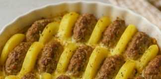 Μια φόρμα ψησίματος με μπιφτέκια και πατάτες κομμένες σε φέτες, τοποθετημένα όρθια σε σειρά, περιχυμένα με κρεμώδη σάλτσα και χρυσαφένια κρούστα τυριού