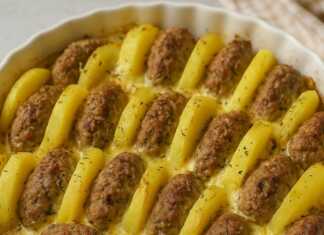 Μια φόρμα ψησίματος με μπιφτέκια και πατάτες κομμένες σε φέτες, τοποθετημένα όρθια σε σειρά, περιχυμένα με κρεμώδη σάλτσα και χρυσαφένια κρούστα τυριού