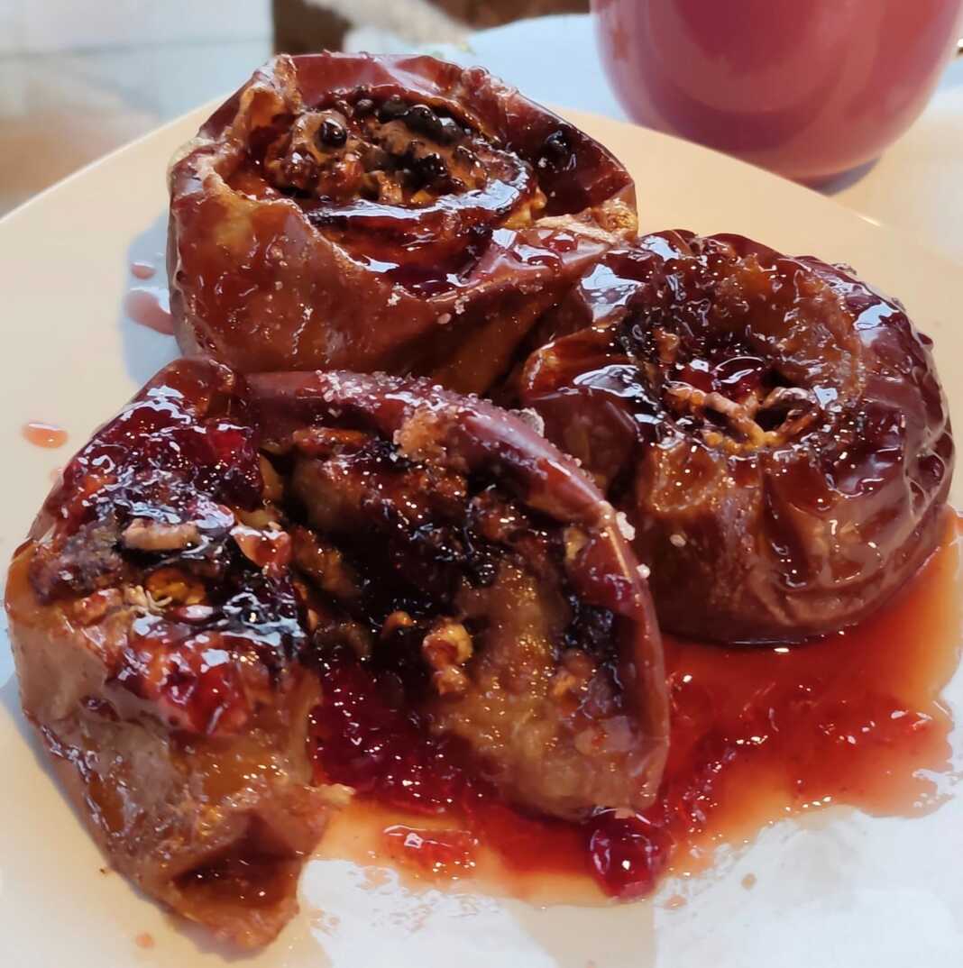 Τέσσερα σιγοψημένα μήλα στο ταψί, κομμένα στη μέση και γεμισμένα με καρύδια και σταφίδες, με σιρόπι από κόκκινο κρασί και κανέλα