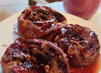 Τέσσερα σιγοψημένα μήλα στο ταψί, κομμένα στη μέση και γεμισμένα με καρύδια και σταφίδες, με σιρόπι από κόκκινο κρασί και κανέλα