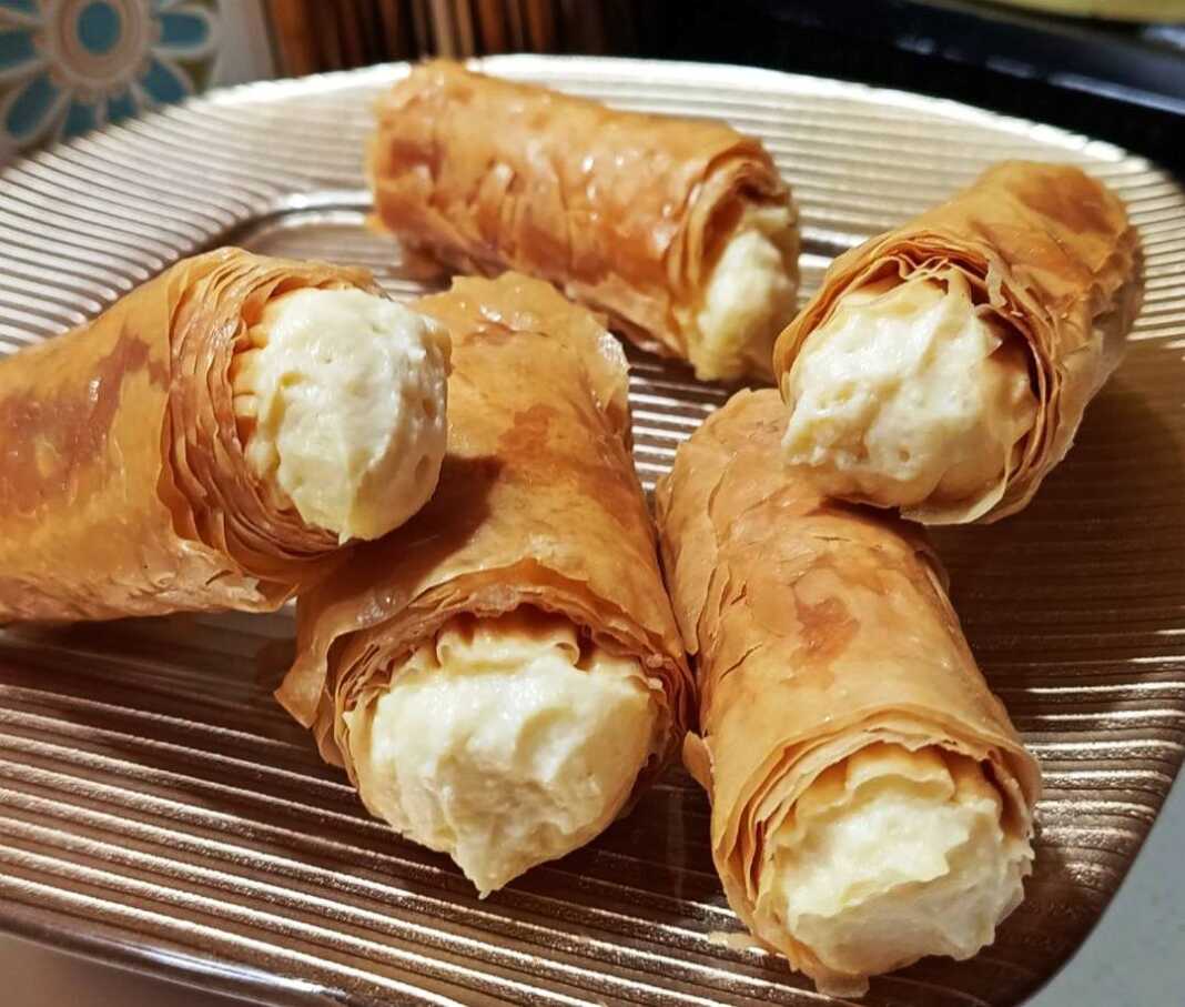 Χρυσαφένια σιροπιαστά ρολάκια κρούστας κορνέ με κρέμα πατισερί, παρουσιασμένα σε πιατέλα