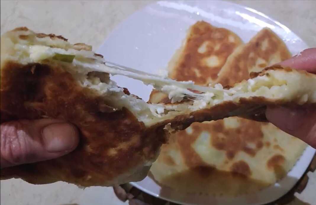 Αφράτες τηγανητές πίτες κομμένες στη μέση που αποκαλύπτουν τη γέμιση τυριού και φρέσκου κρεμμυδιού