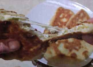 Αφράτες τηγανητές πίτες κομμένες στη μέση που αποκαλύπτουν τη γέμιση τυριού και φρέσκου κρεμμυδιού