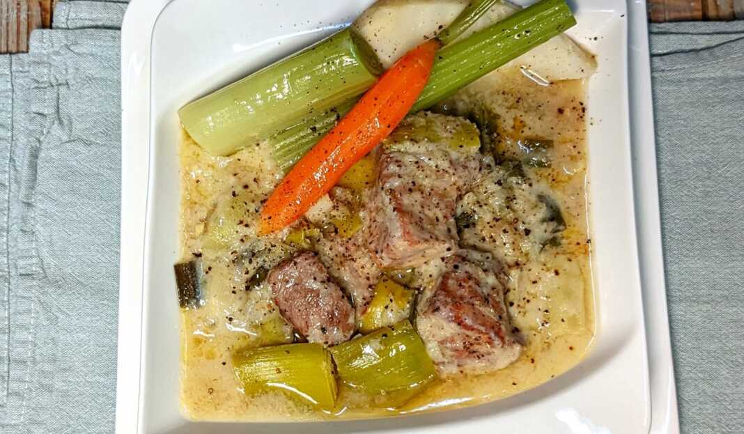 Χοιρινό με πρασοσέλινο με αυγολέμονο, σερβιρισμένο σε πιάτο με την παχύρρευστη λευκή σάλτσα