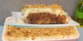 Ένα πλούσιο κομμάτι παραδοσιακής πουτίγκας με στρώσεις καρυδόπιτας, σοκολάτας και λευκής κρέμας, πασπαλισμένο με κανέλα.