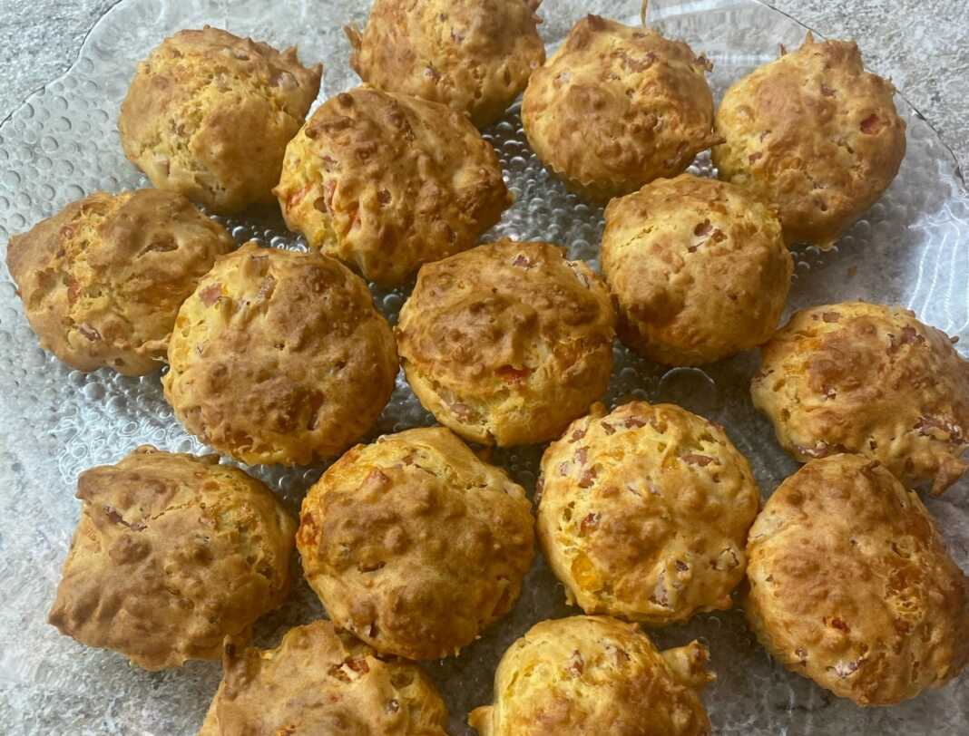 Δώδεκα αλμυρά μάφινς με κοτόπουλο, τυρί και κόκκινα κομμάτια ντομάτας, σερβιρισμένα σε καλαθάκια για μάφινς