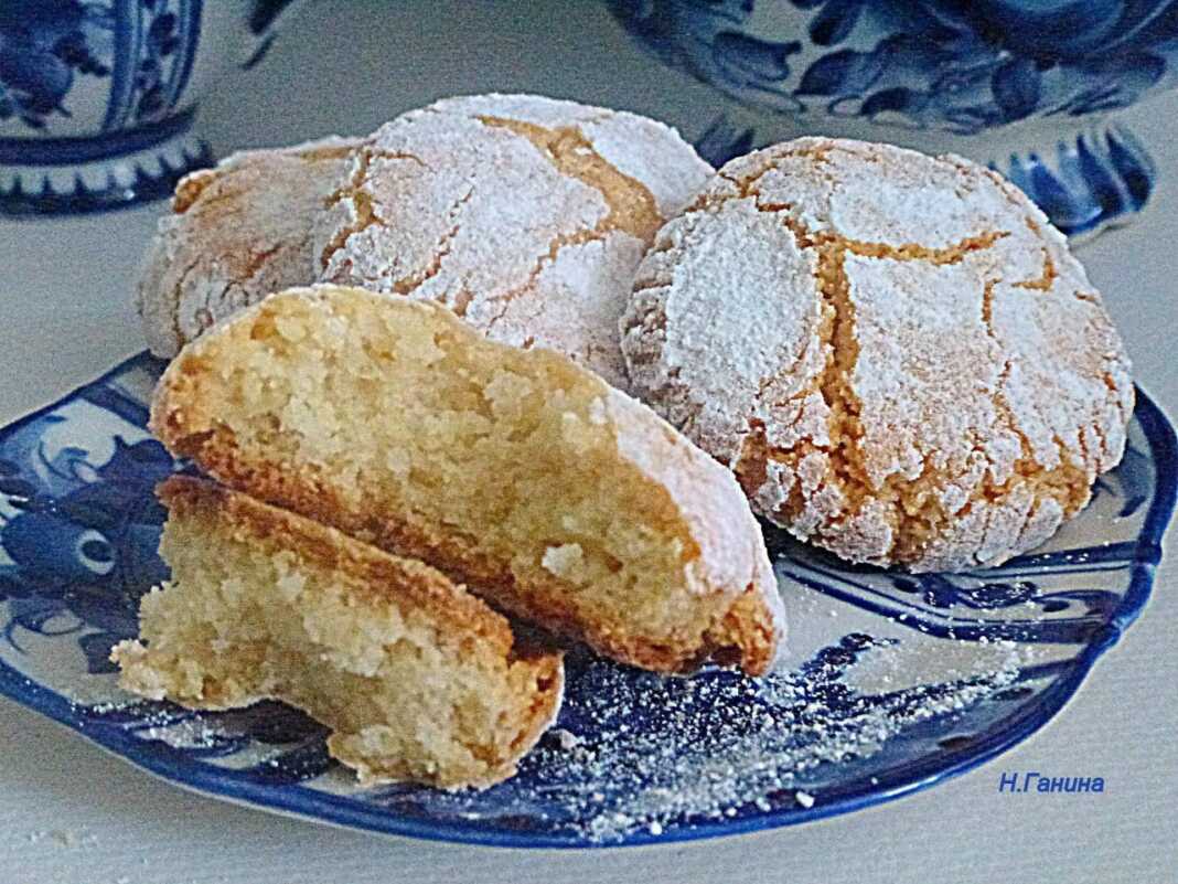 Μια σειρά από χιονισμένα αμυγδαλωτά μπισκότα πασπαλισμένα με ζάχαρη άχνη πάνω σε γιορτινό φόντο.