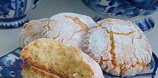 Μια σειρά από χιονισμένα αμυγδαλωτά μπισκότα πασπαλισμένα με ζάχαρη άχνη πάνω σε γιορτινό φόντο.