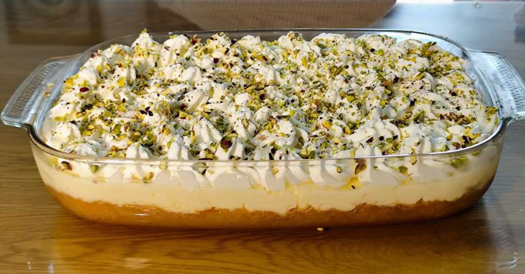 Ένα πλούσιο κομμάτι εκμέκ κανταΐφι με στρώσεις από σιροπιασμένη βάση, κρέμα και σαντιγί, πασπαλισμένο με πράσινο φιστίκι Αιγίνης.