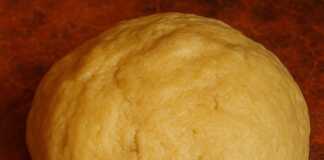 Μια μπάλα φρέσκιας ζύμης πάνω σε αλευρωμένη επιφάνεια εργασίας, δίπλα σε ένα πλάστη και κομμάτια βουτύρου.