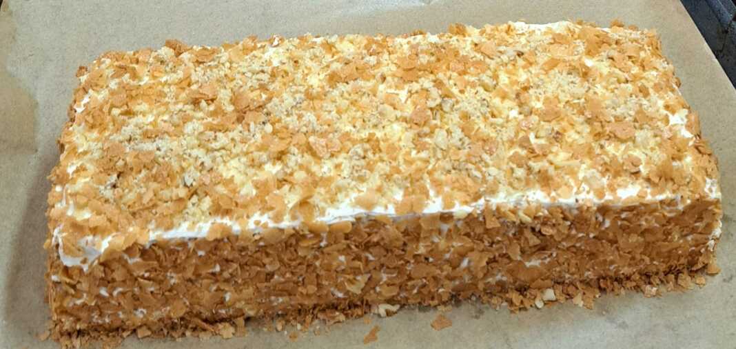 Ένα λαχταριστό κέικ καρότου με τρεις στρώσεις, καλυμμένο με λευκή κρέμα τυριού και πασπαλισμένο με καρύδια και ψίχουλα.