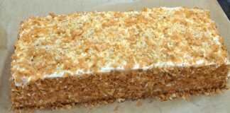 Ένα λαχταριστό κέικ καρότου με τρεις στρώσεις, καλυμμένο με λευκή κρέμα τυριού και πασπαλισμένο με καρύδια και ψίχουλα.