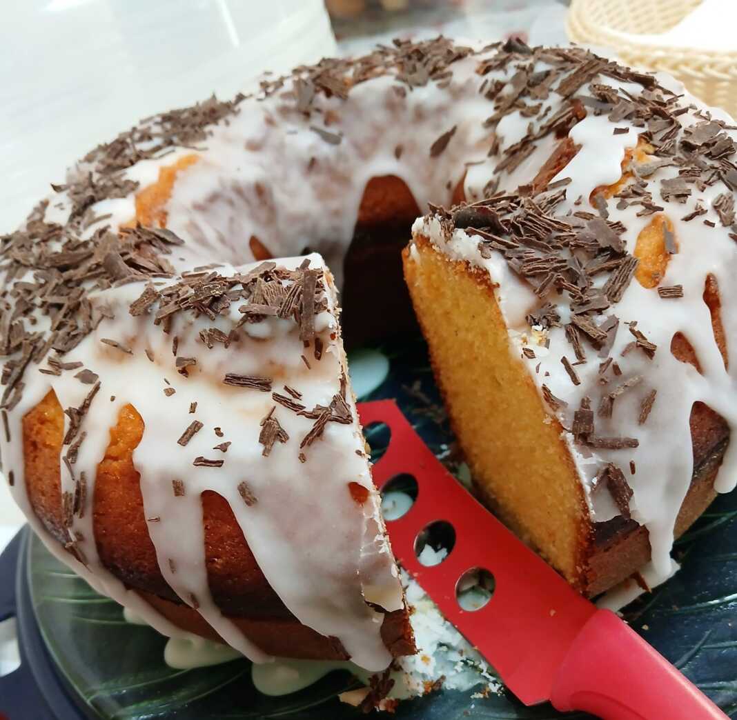 Ένα ψηλό, χρυσαφένιο κέικ μανταρίνι σε φόρμα, γαρνιρισμένο με άχνη ζάχαρη και φέτες από φρέσκο μανταρίνι.