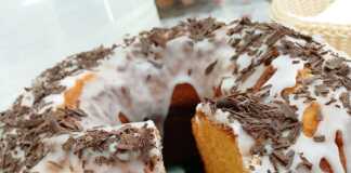 Ένα ψηλό, χρυσαφένιο κέικ μανταρίνι σε φόρμα, γαρνιρισμένο με άχνη ζάχαρη και φέτες από φρέσκο μανταρίνι.