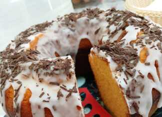 Ένα ψηλό, χρυσαφένιο κέικ μανταρίνι σε φόρμα, γαρνιρισμένο με άχνη ζάχαρη και φέτες από φρέσκο μανταρίνι.