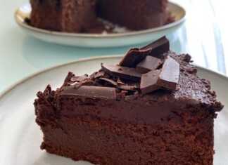 Ένα πλούσιο σκούρο κέικ σοκολάτας χωρίς αλεύρι, περιχυμένο με γλάσο σοκολάτας και διακοσμημένο με ξύσμα σοκολάτας (στροβιλισμούς).