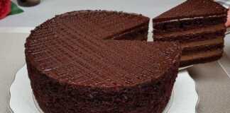 Ένα πλούσιο κέικ σοκολάτας με πολλές στρώσεις κρέμας, καλυμμένο με γυαλιστερό γλάσο και τριμμένο κέικ στα πλαϊνά.