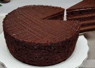 Ένα πλούσιο κέικ σοκολάτας με πολλές στρώσεις κρέμας, καλυμμένο με γυαλιστερό γλάσο και τριμμένο κέικ στα πλαϊνά.