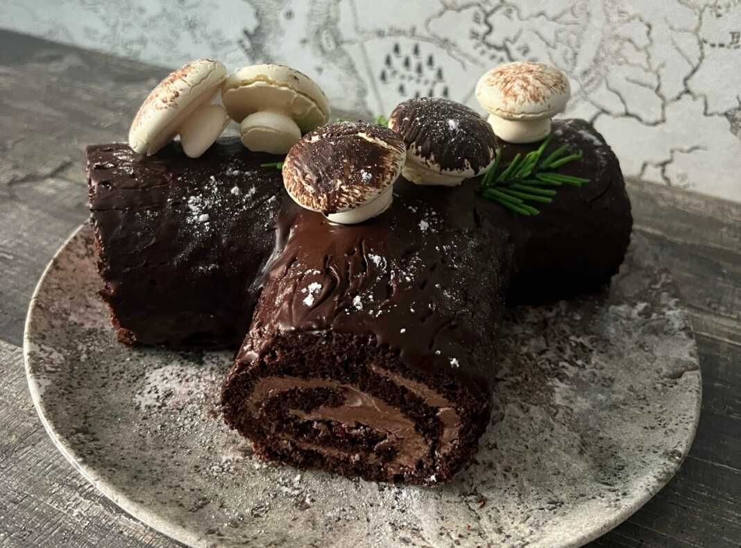 Ένας σοκολατένιος κορμός Χριστουγέννων διακοσμημένος με γλάσο σοκολάτας, μανιτάρια από μαρέγκα και άχνη ζάχαρη.