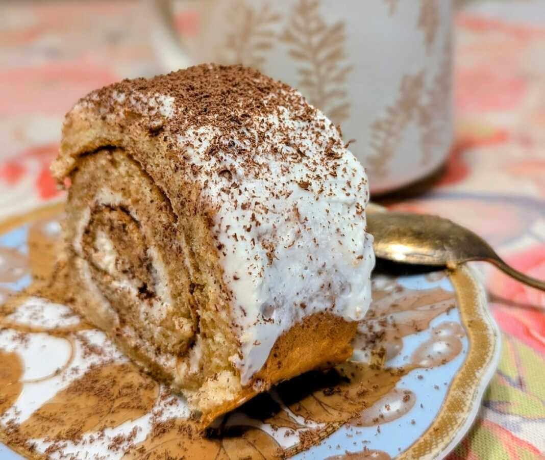 Ένα εντυπωσιακό ρολό τιραμισού πασπαλισμένο με κακάο, κομμένο σε φέτες που δείχνουν την πλούσια κρέμα και το εμποτισμένο με καφέ παντεσπάνι.