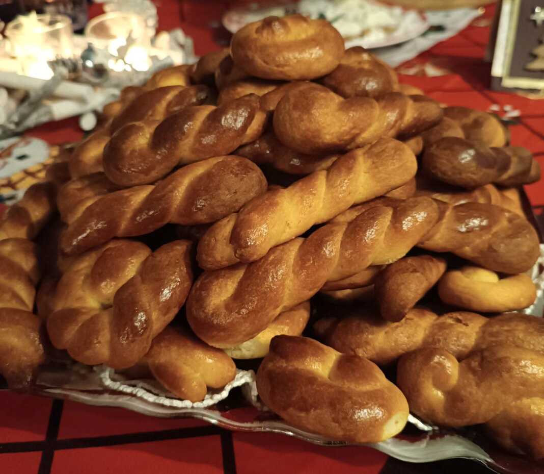 Κουλουράκια σε διάφορα σχήματα (πλεξούδες, στρόγγυλα), με χρυσαφί επιφάνεια από επάλειψη αυγού, τοποθετημένα σε ταψί.