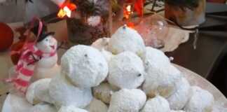 Σειρές από χιονισμένους κουραμπιέδες με άφθονη άχνη ζάχαρη, τοποθετημένους σε γιορτινή πιατέλα.