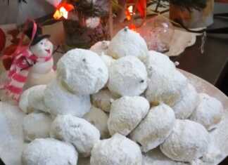 Σειρές από χιονισμένους κουραμπιέδες με άφθονη άχνη ζάχαρη, τοποθετημένους σε γιορτινή πιατέλα.