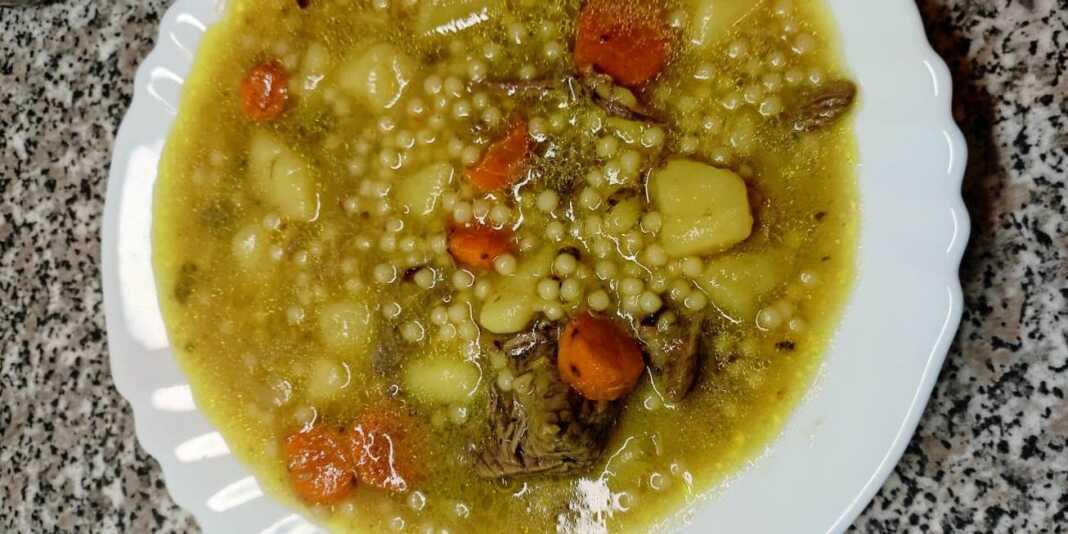 Ένα μεγάλο μπολ γεμάτο με ζεστή κρεατόσουπα μοσχαριού με κομμάτια λαχανικών και κουσκουσάκι, με λίγο πιπέρι στην επιφάνεια.