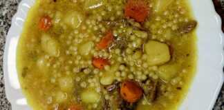 Ένα μεγάλο μπολ γεμάτο με ζεστή κρεατόσουπα μοσχαριού με κομμάτια λαχανικών και κουσκουσάκι, με λίγο πιπέρι στην επιφάνεια.