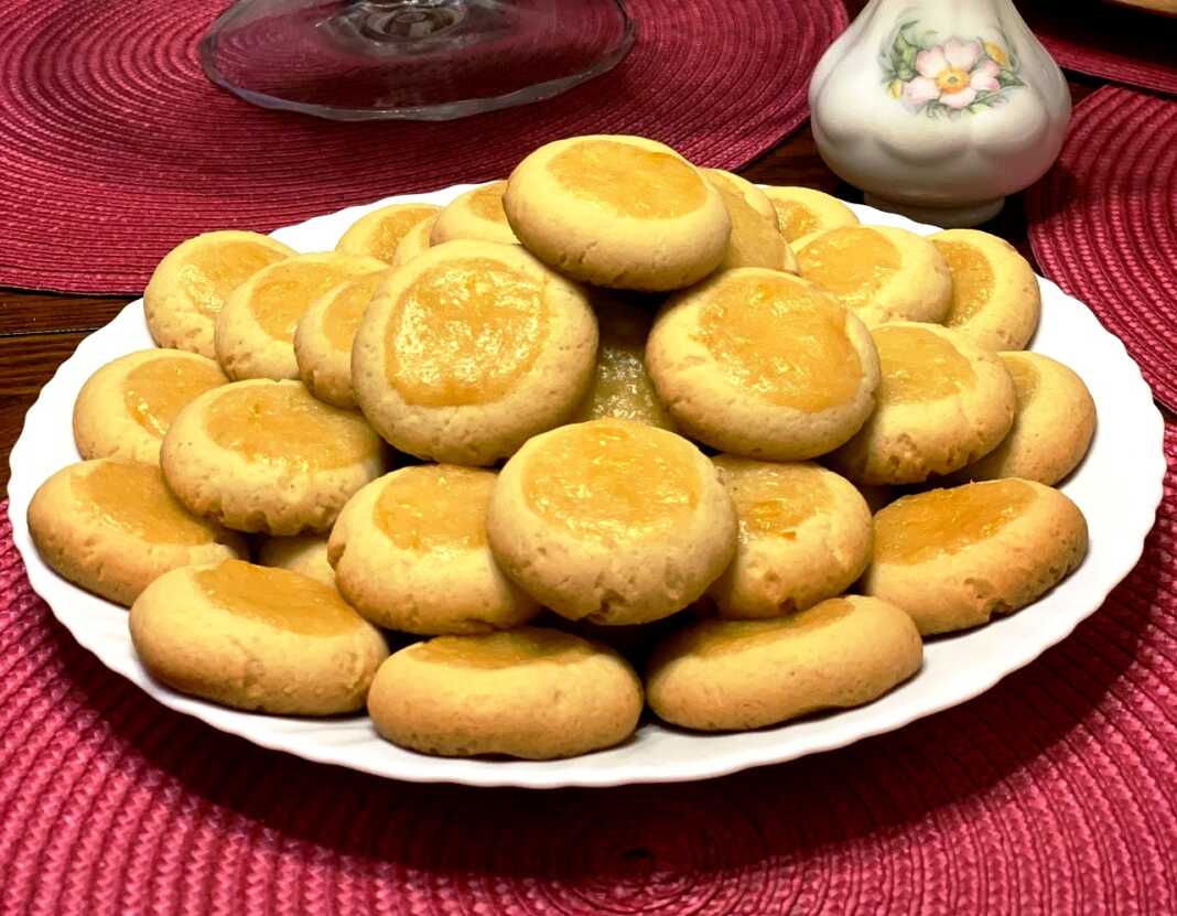 Φωτογραφία από μια πιατέλα με στρογγυλά μπισκότα βουτύρου (μπισκότα "Μάτια"), γεμισμένα στο κέντρο με κίτρινη λαμπερή κρέμα λεμονιού και ελαφρώς πασπαλισμένα με ζάχαρη άχνη.