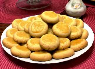 Φωτογραφία από μια πιατέλα με στρογγυλά μπισκότα βουτύρου (μπισκότα "Μάτια"), γεμισμένα στο κέντρο με κίτρινη λαμπερή κρέμα λεμονιού και ελαφρώς πασπαλισμένα με ζάχαρη άχνη.