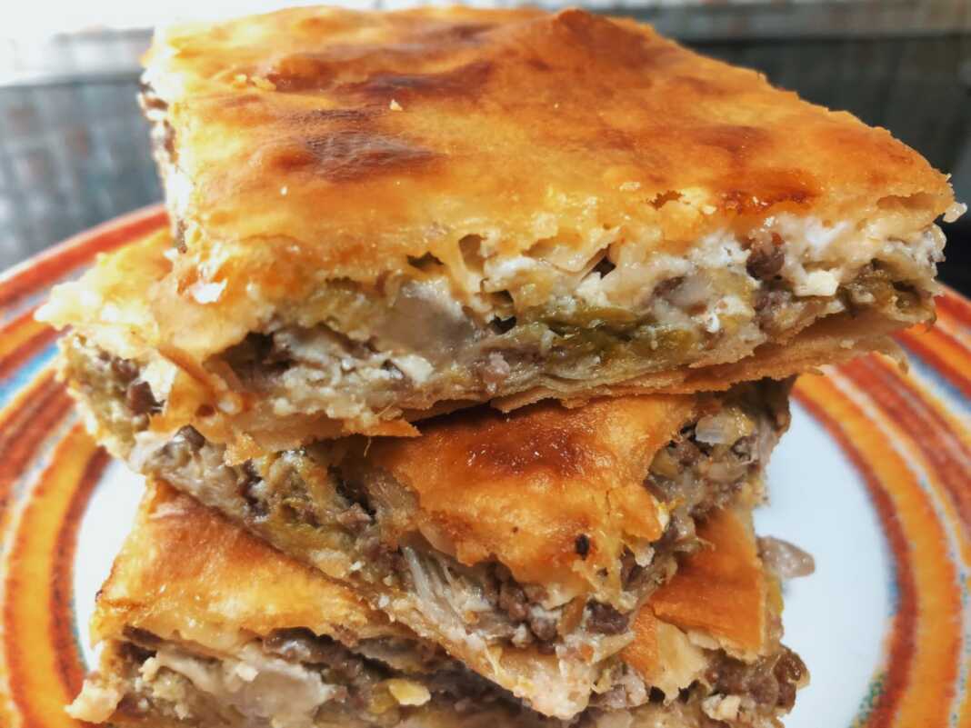 Μια λαχταριστή πρασόπιτα με κιμά σε ορθογώνιο ταψί, κομμένη σε τετράγωνα κομμάτια και ροδοκοκκινισμένη.