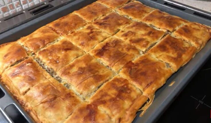 Μια λαχταριστή πρασόπιτα με κιμά σε ορθογώνιο ταψί, κομμένη σε τετράγωνα κομμάτια και ροδοκοκκινισμένη.